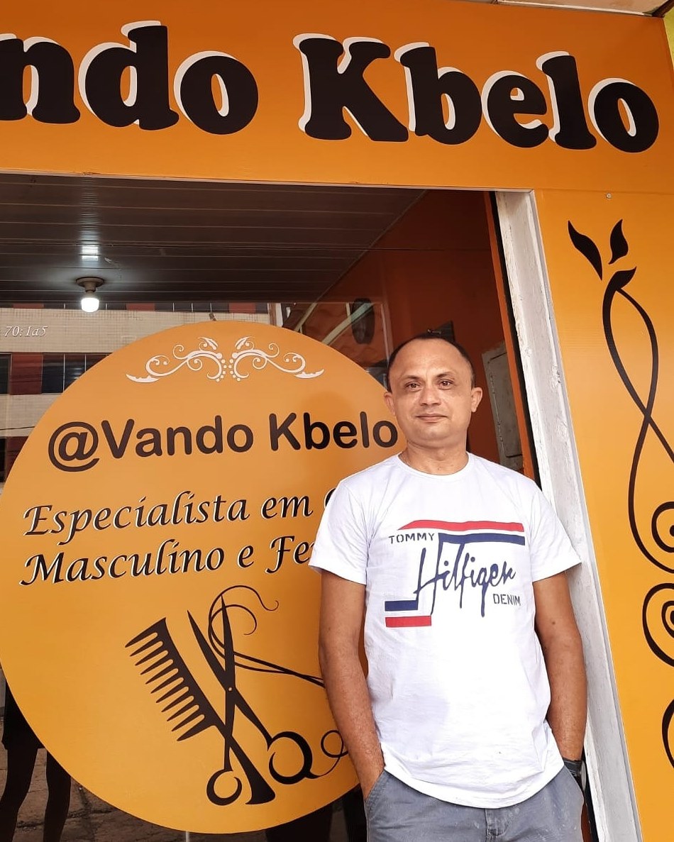O cabeleireiro Vando na entrada do salão, sob a placa @Vando Kbelo